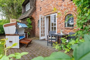 Een huis van baksteen met rieten dak, een houten bank, een tafel en een stoel.