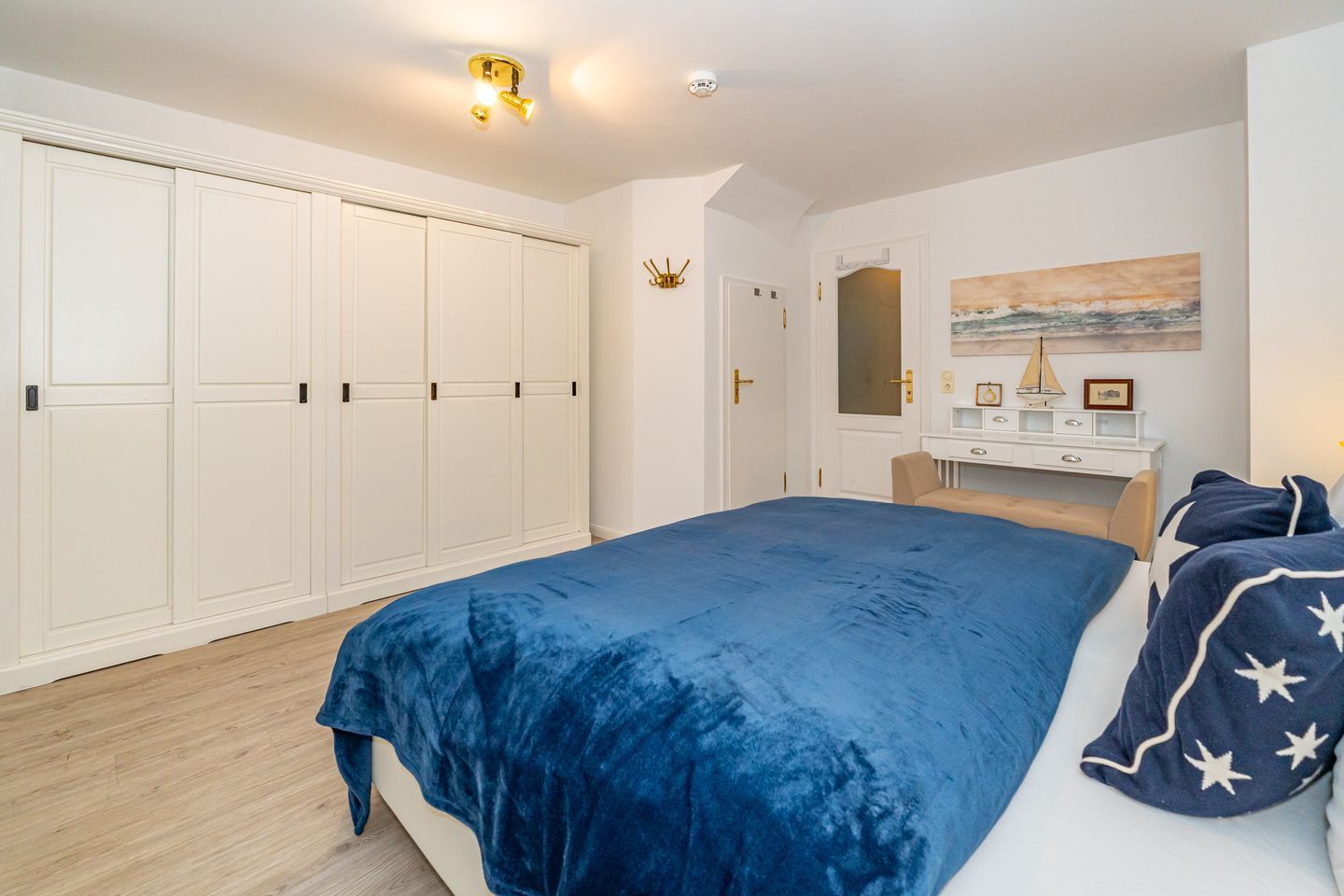 Ein Schlafzimmer mit einem großen Bett, einem Kleiderschrank, einem Schreibtisch und einem Bild an der Wand.