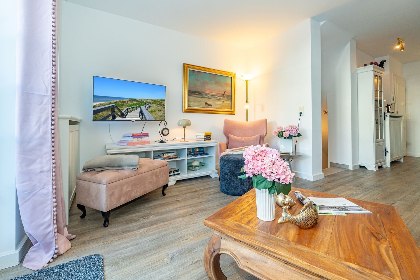 Ein Wohnzimmer mit einer Couch, einem Couchtisch mit Blumen, einem Bücherregal und einem Bild an der Wand.