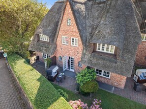 A traditional thatched-roof house with a brick exterior, a patio with outdoor furniture, and a well-maintained garden. - Altstadttor 17 - Holiday apartment under thatch for up to two people in (Sylt)