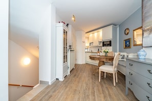 A compact kitchen with white cabinetry, a wooden dining table, and a blue vase on a dresser. - Altstadttor 17 - Holiday apartment under thatch for up to two people in (Sylt)