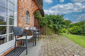 A brick building with a thatched roof, a wooden fence, and a paved patio with a table and chairs. - Altstadttor 17 - Holiday apartment under thatch for up to two people in (Sylt)