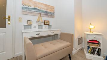 A room with a beige bench, a white desk with drawers, a bookshelf, and a painting of a seascape.