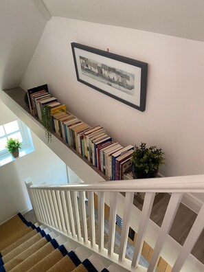 Una escalera con barandilla blanca, una fila de libros en la pared y un cuadro enmarcado encima.