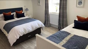 A bedroom with two beds, a window with curtains, a radiator, and a lamp on a bedside table.