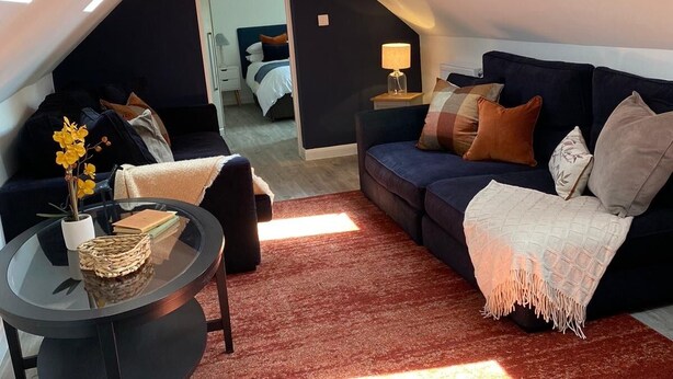 An attic room with a dark-colored sofa, a round glass coffee table, and a red rug.