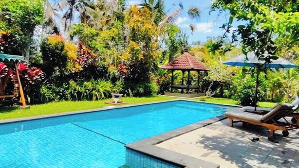 A swimming pool with a gazebo, surrounded by lush greenery and palm trees. - Madesimon Villa (Payangan)