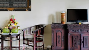 A room with a wooden cabinet, a television, and a table with a floral arrangement and two green fruits. - Madesimon Villa (Payangan)
