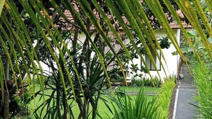 A pathway flanked by lush greenery and a building with a tiled roof. - Madesimon Villa (Payangan)