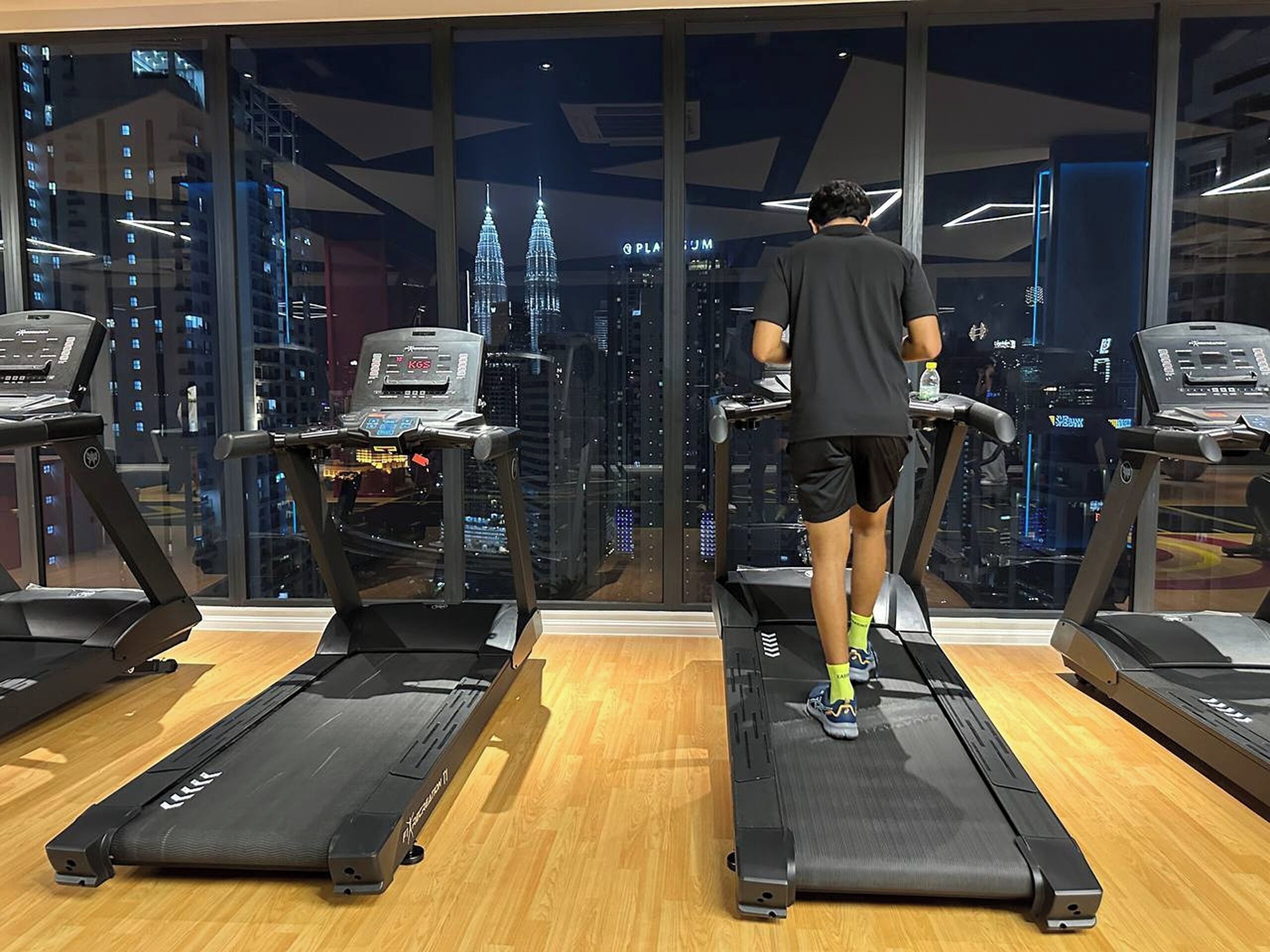 A gym with treadmills, a digital display, and a city view.