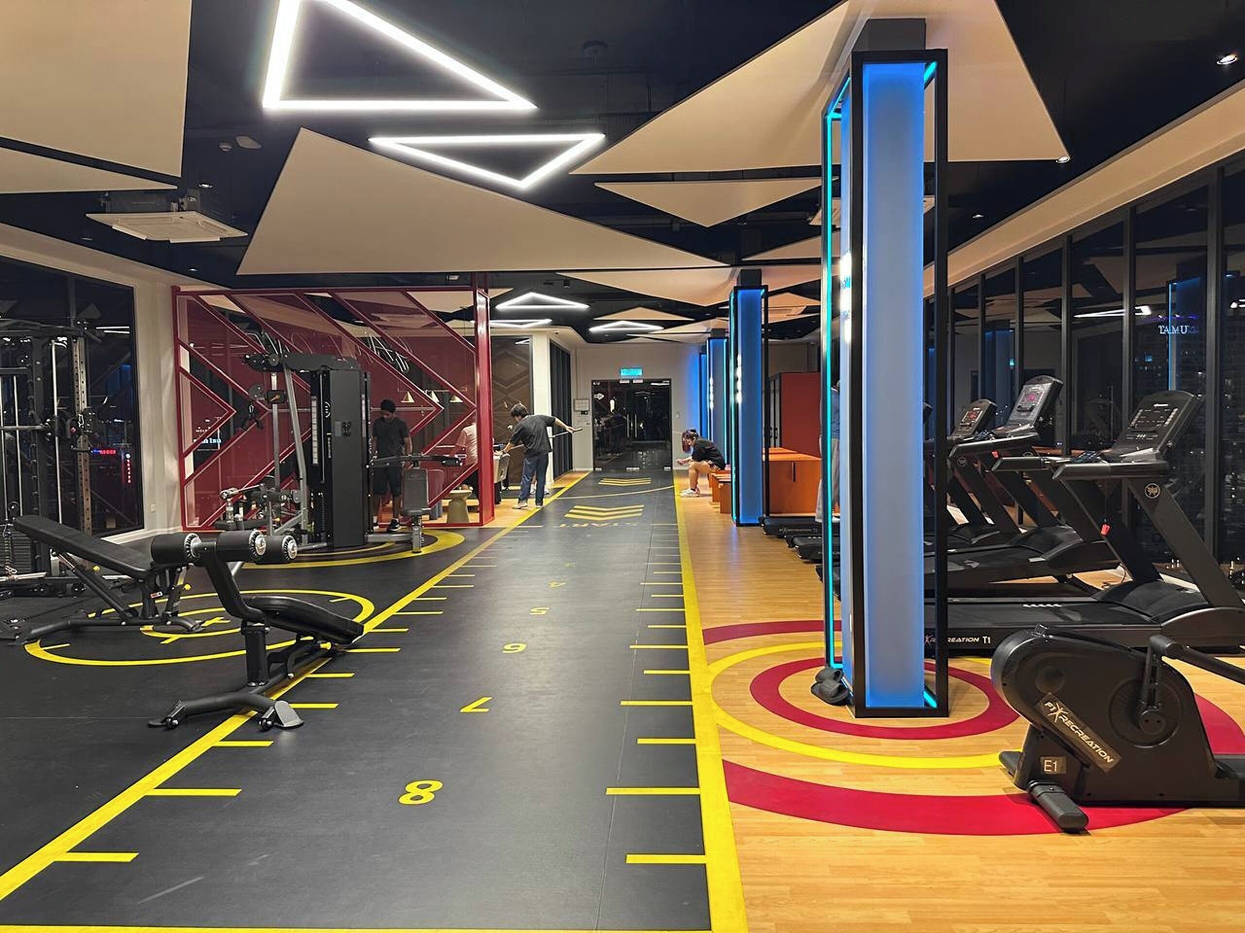 Une salle de sport équipée de tapis de course, d’appareils de musculation et dotée d’un sol jaune portant des numéros.