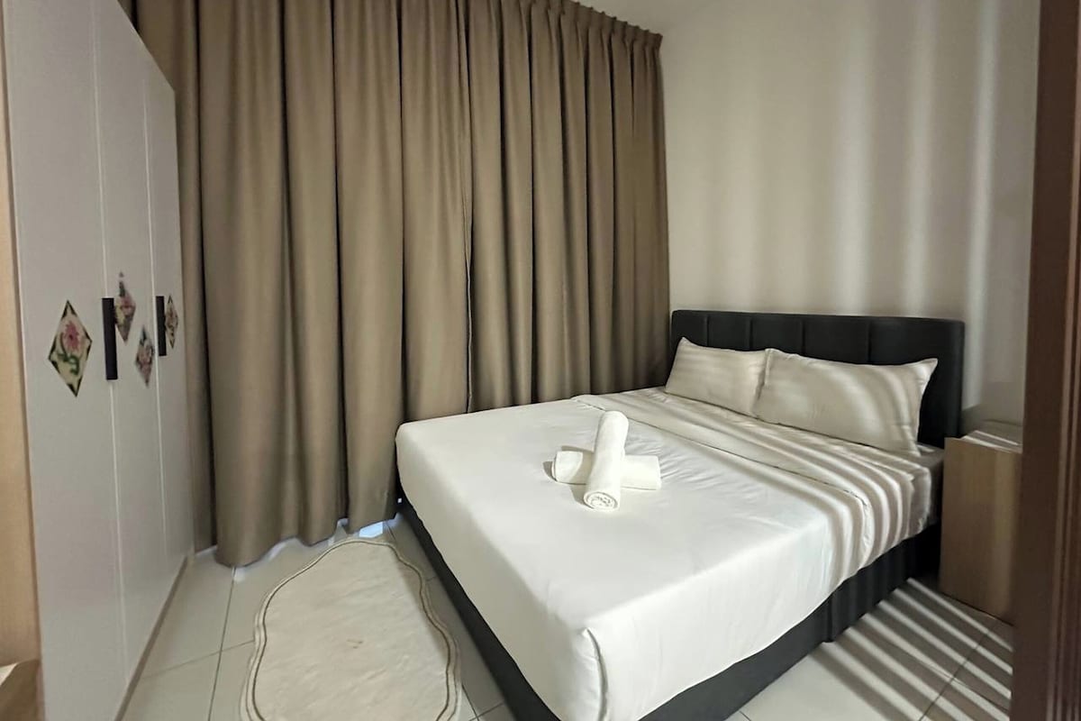 Ein Hotelzimmer mit einem großen Bett, beigen Vorhängen und einem ordentlich bezogenen Bett mit einem Handtuch.