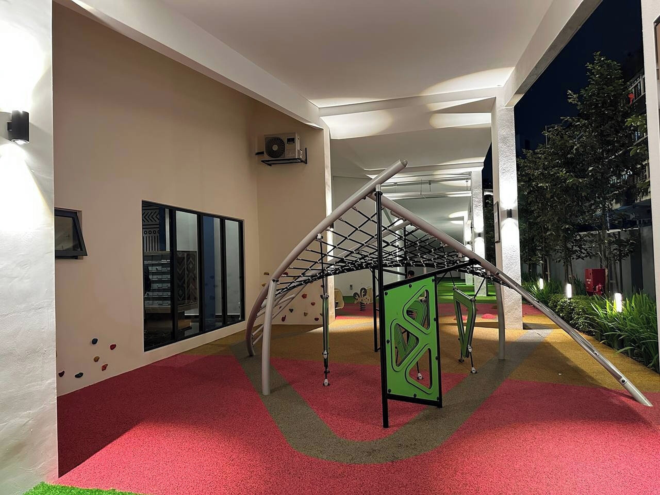 Un área de juegos interior moderna con una estructura de escalada, suelo de césped artificial y una pared de vidrio con diseño geométrico.
