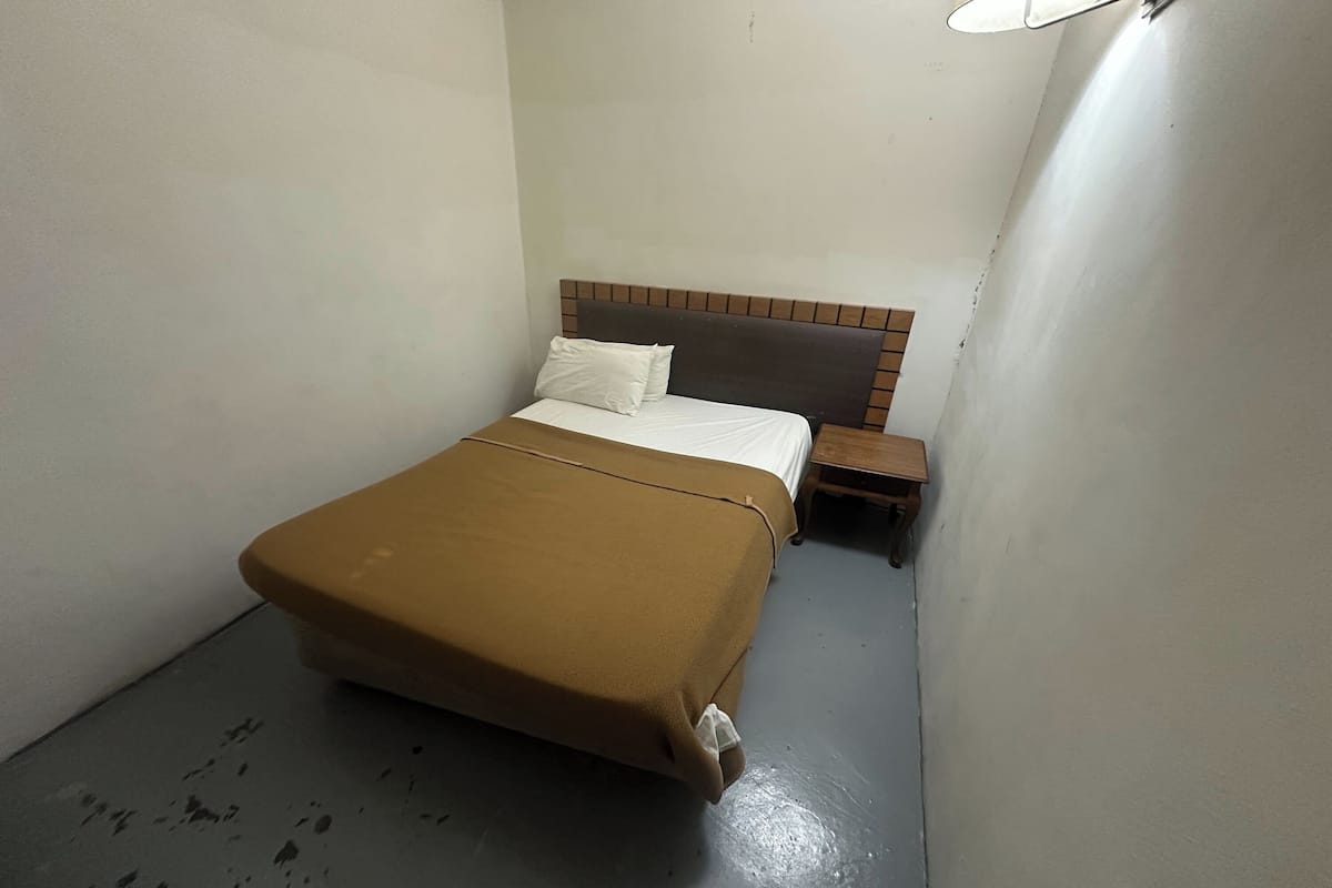 Una habitación de hotel pequeña y estrecha con una cama individual, una mesita de noche y una lámpara fijada a la pared.