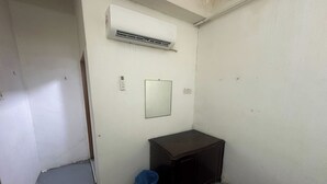 A small, narrow room with a white door, a blue trash bin, a dark wooden cabinet, and an air conditioning unit mounted on the wall. - Hotel No.1 Lodge (Nilai)