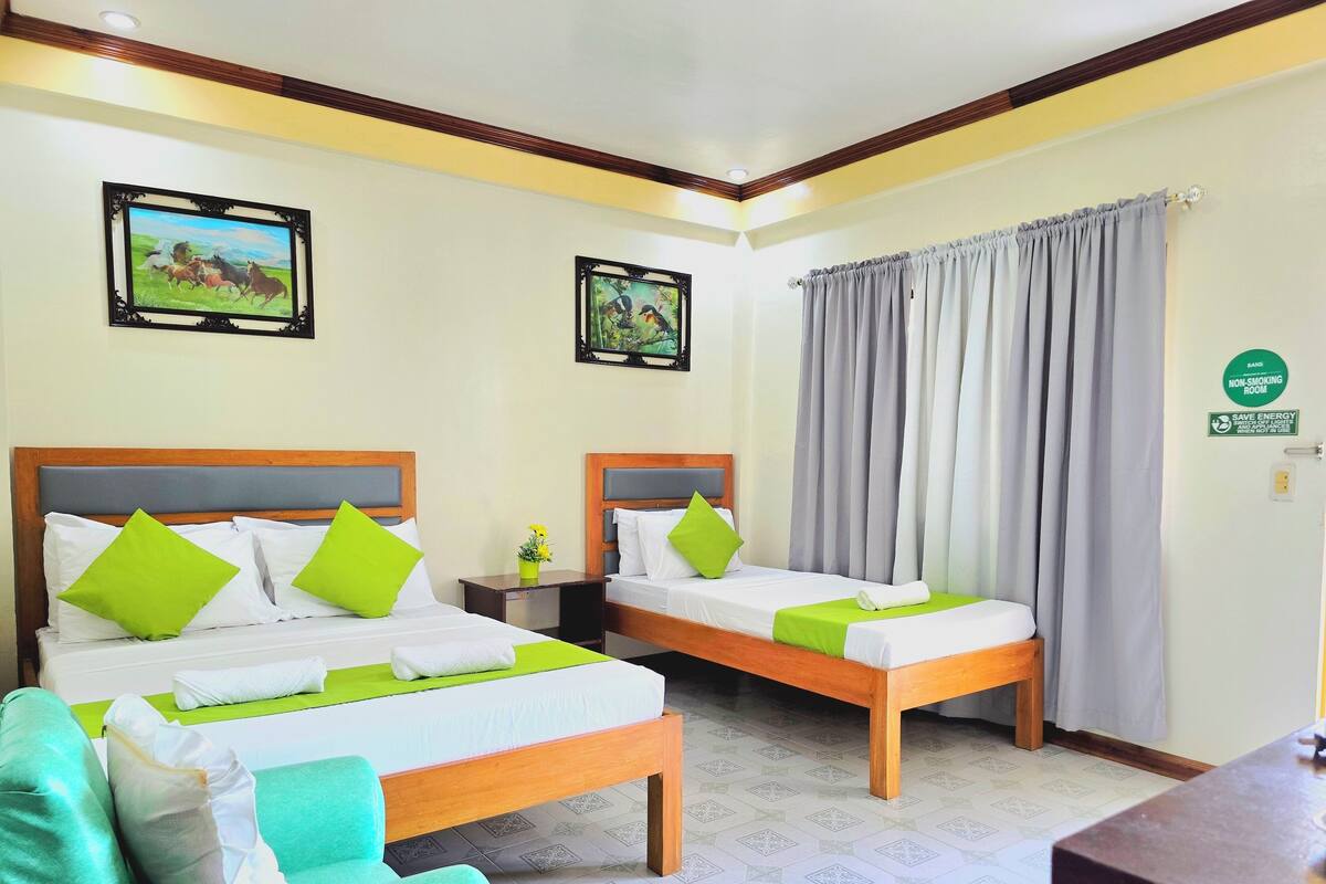 A hotel room with two beds, green and white bedding, a green chair, and a painting on the wall.