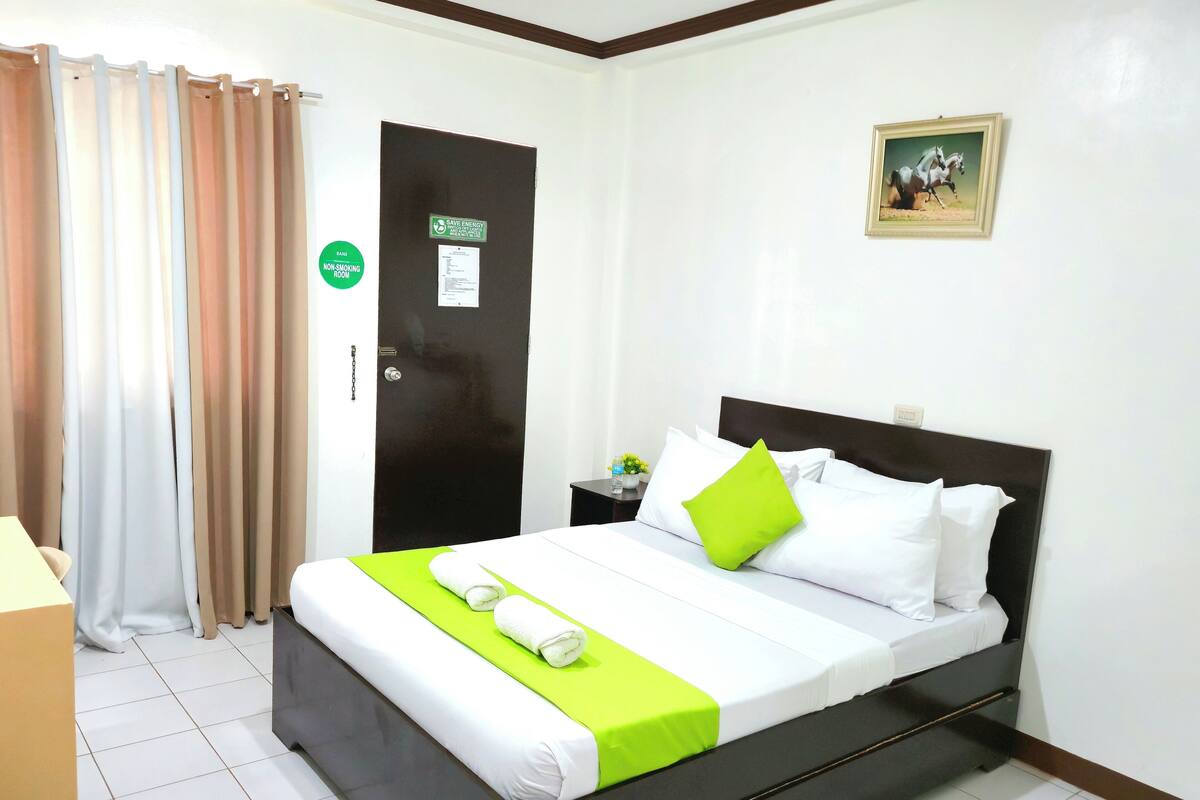 A hotel room with a bed, a nightstand, a door, and a picture on the wall.