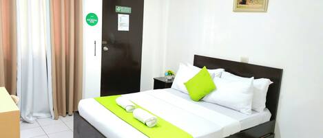 A hotel room with a bed, a nightstand, a door, and a picture on the wall.