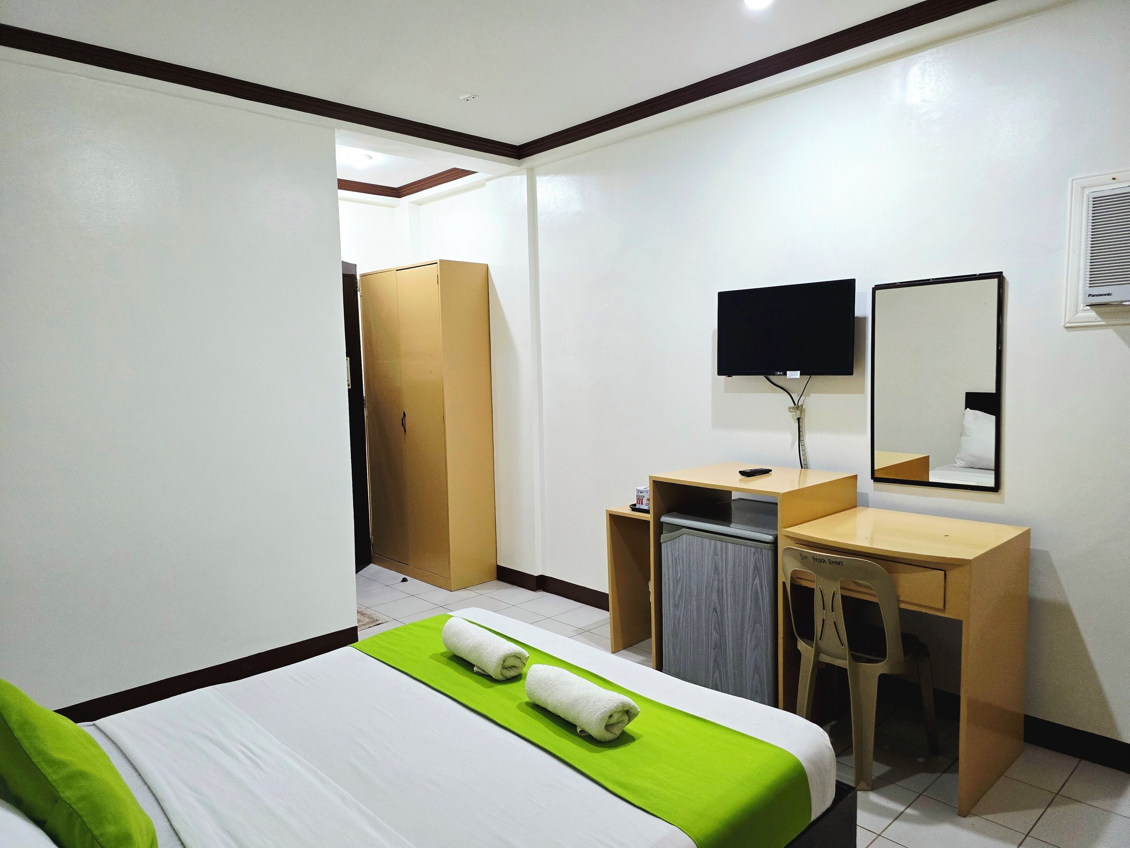 A hotel room with a bed, a desk, a chair, a wardrobe, a television, and a mirror.