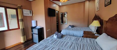 A hotel room with two beds, a desk, a mirror, a lamp, and a television.