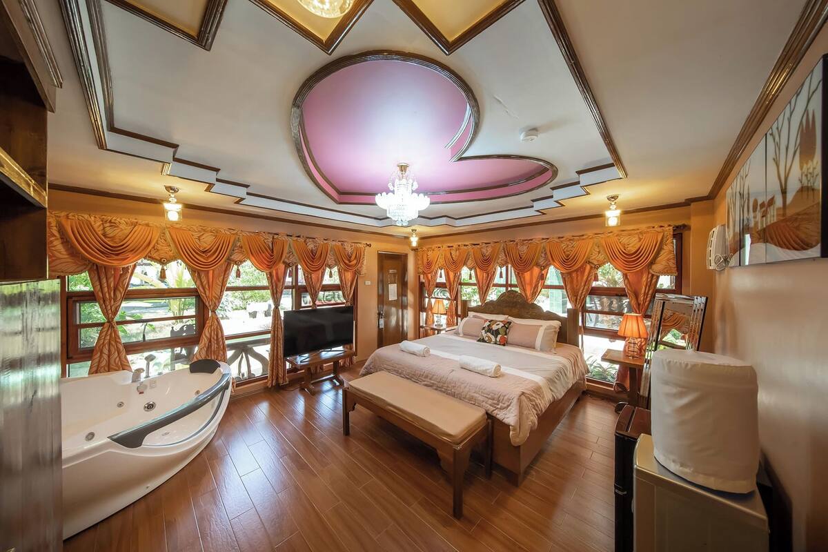 A spacious bedroom with a large bed, a bathtub, and a television.