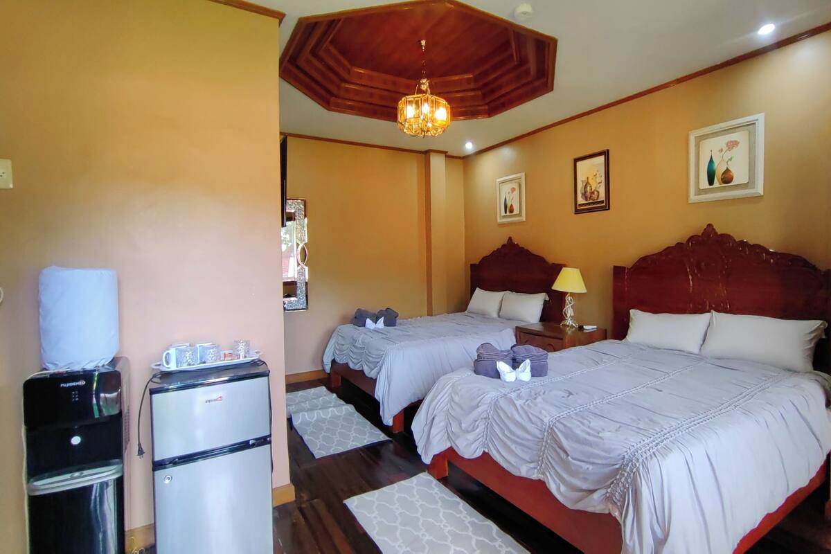 A hotel room with two beds, a refrigerator, a water dispenser, and a ceiling light fixture.