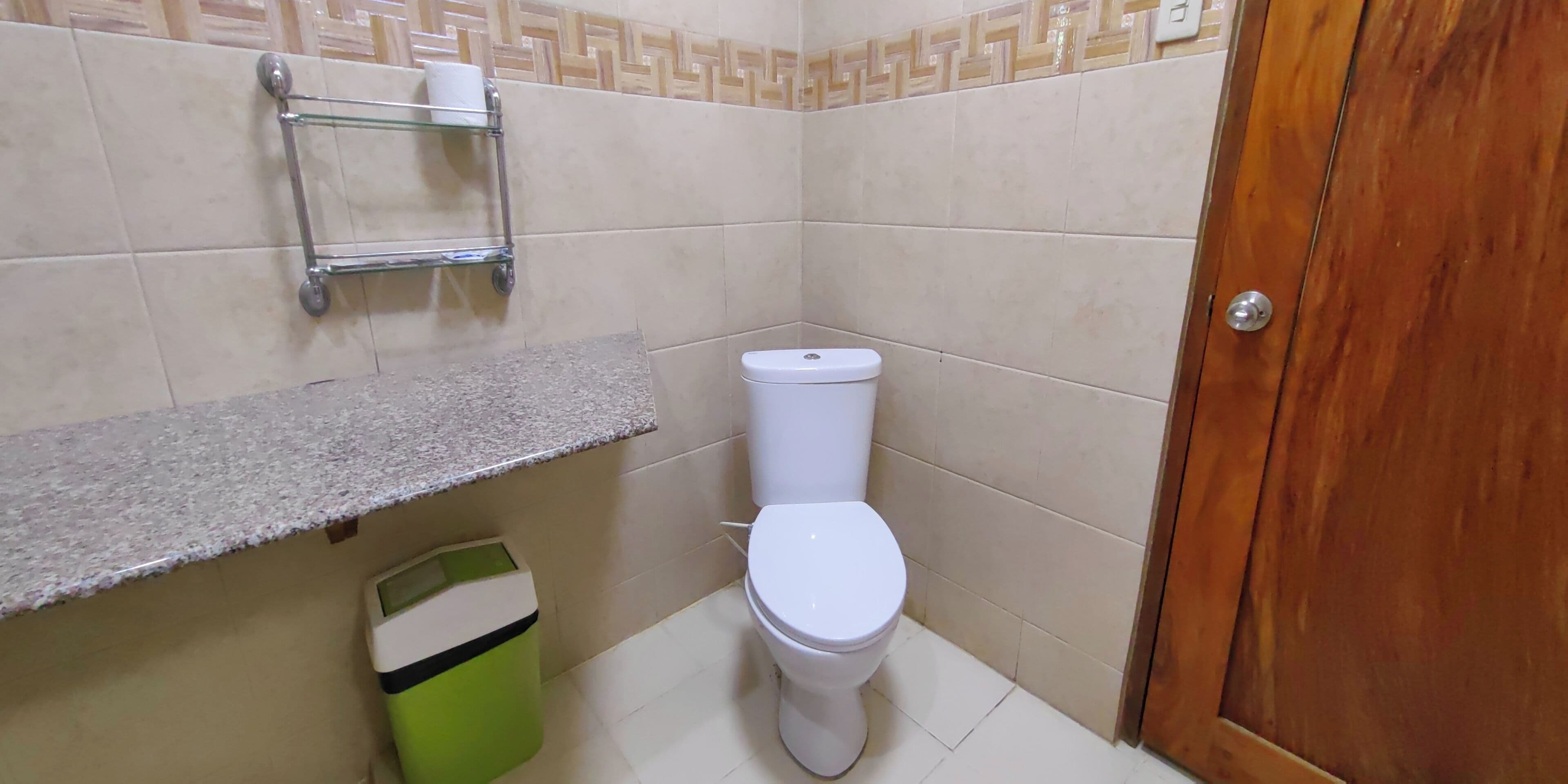 Une salle de bain équipée de toilettes, d’une poubelle, d’un porte-serviettes et d’un lavabo.