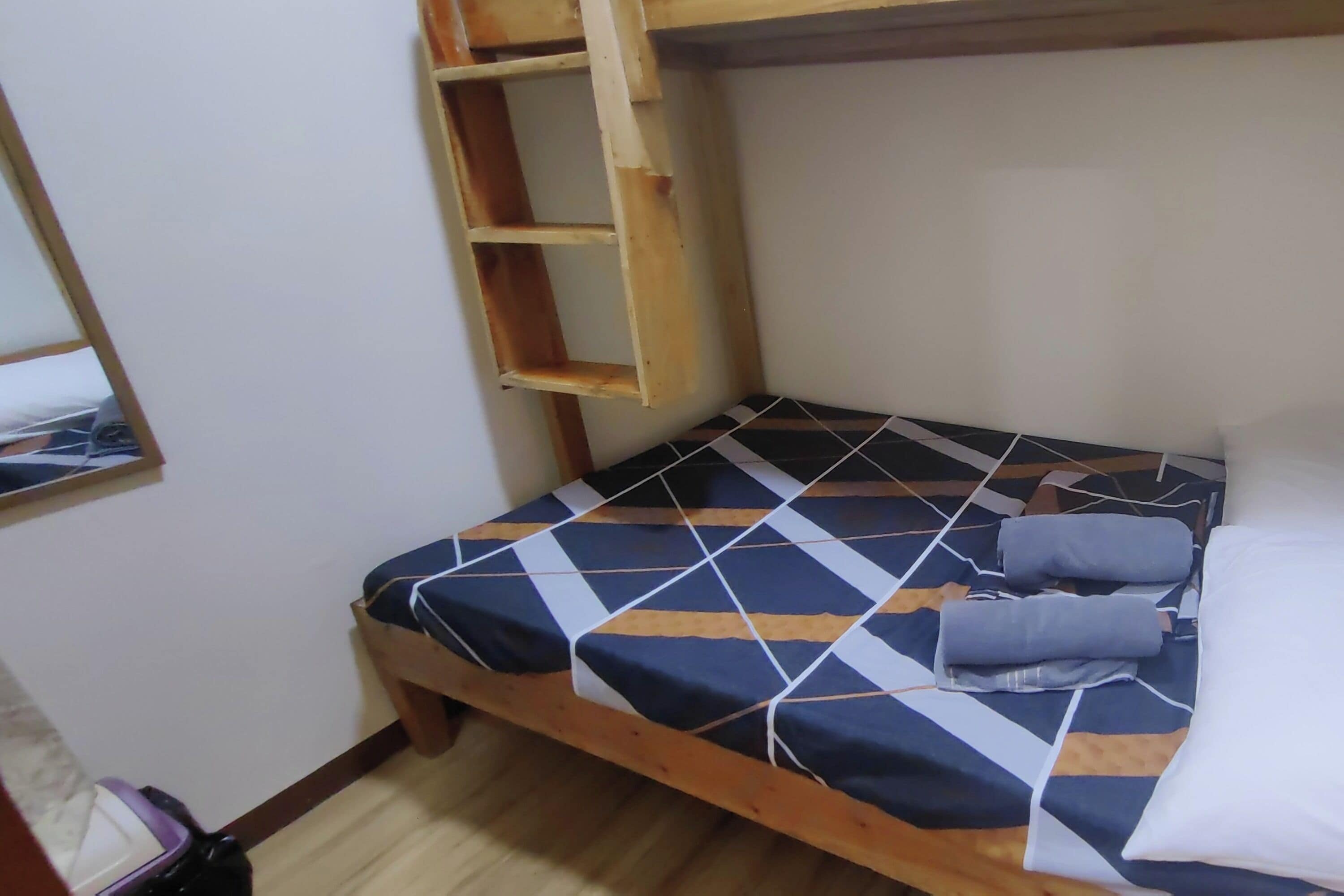 Un lit simple avec une couvre-lit à motifs géométriques, une tête de lit en bois et une petite étagère.