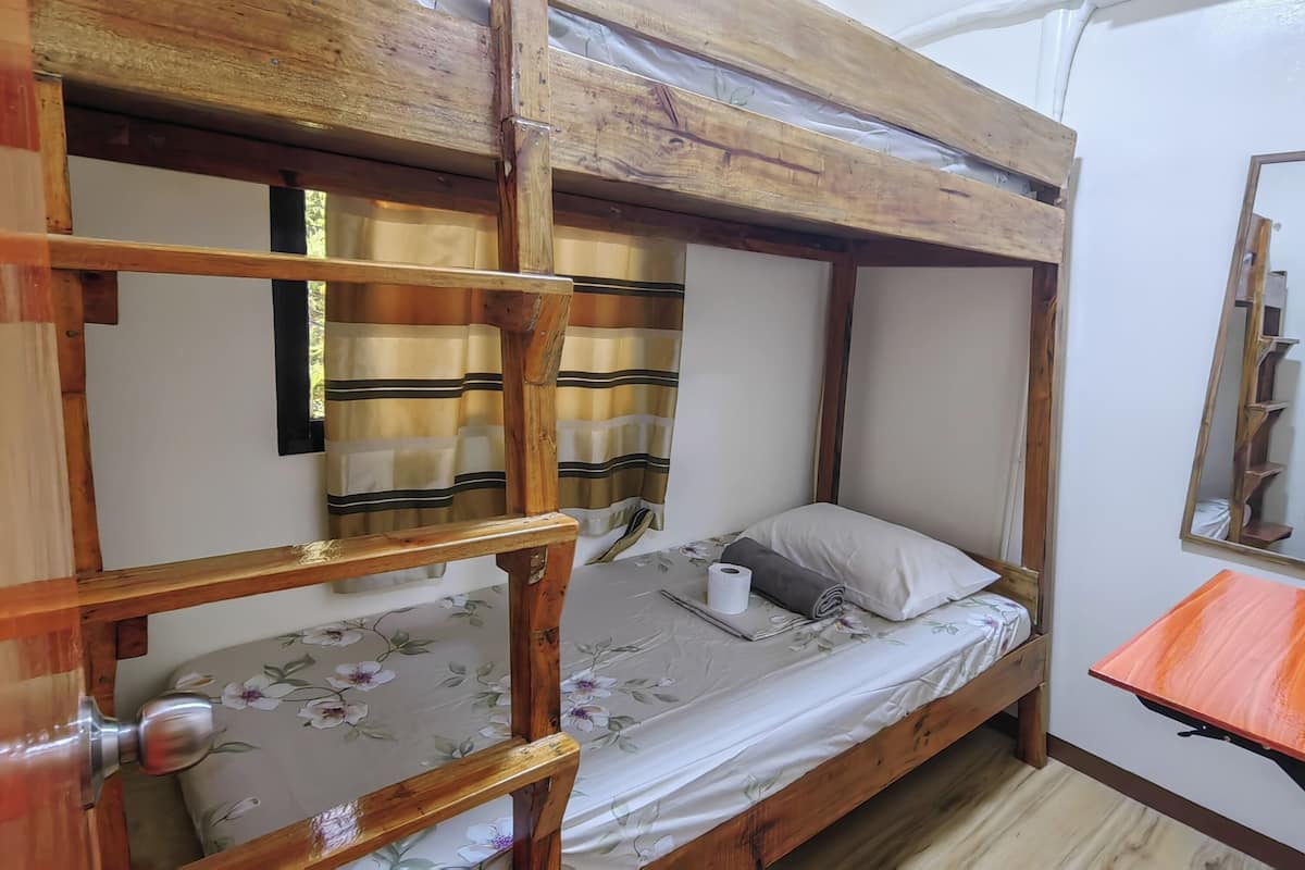 Ein Stockbett mit Holzrahmen, ein Einzelbett darunter, ein kleiner Tisch und ein Spiegel an der Wand.