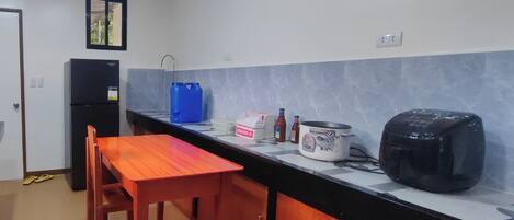 A compact kitchen with a refrigerator, a blue water dispenser, a rice cooker, and a toaster.