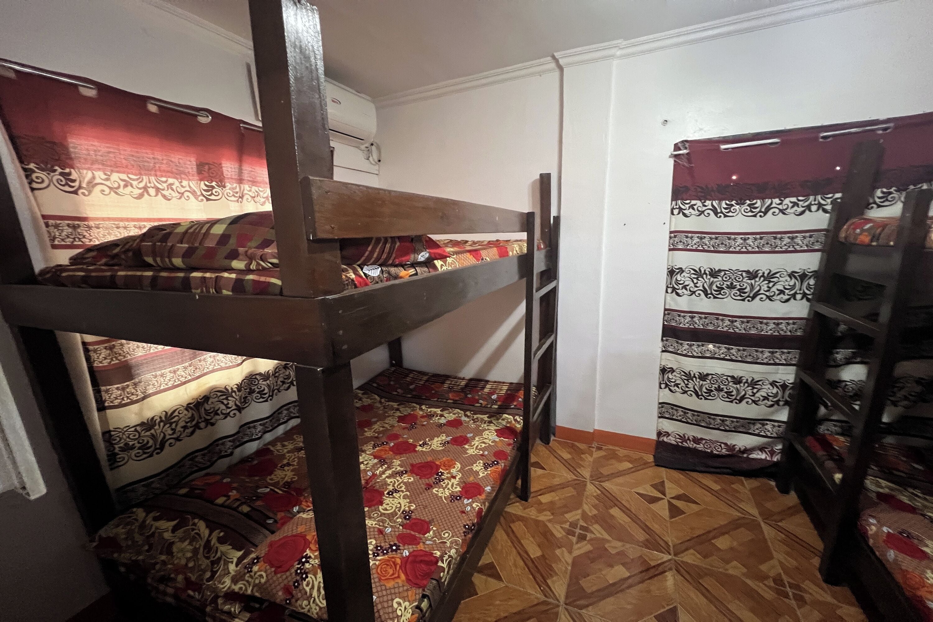 A dormitory room with bunk beds, patterned curtains, and a tiled floor.