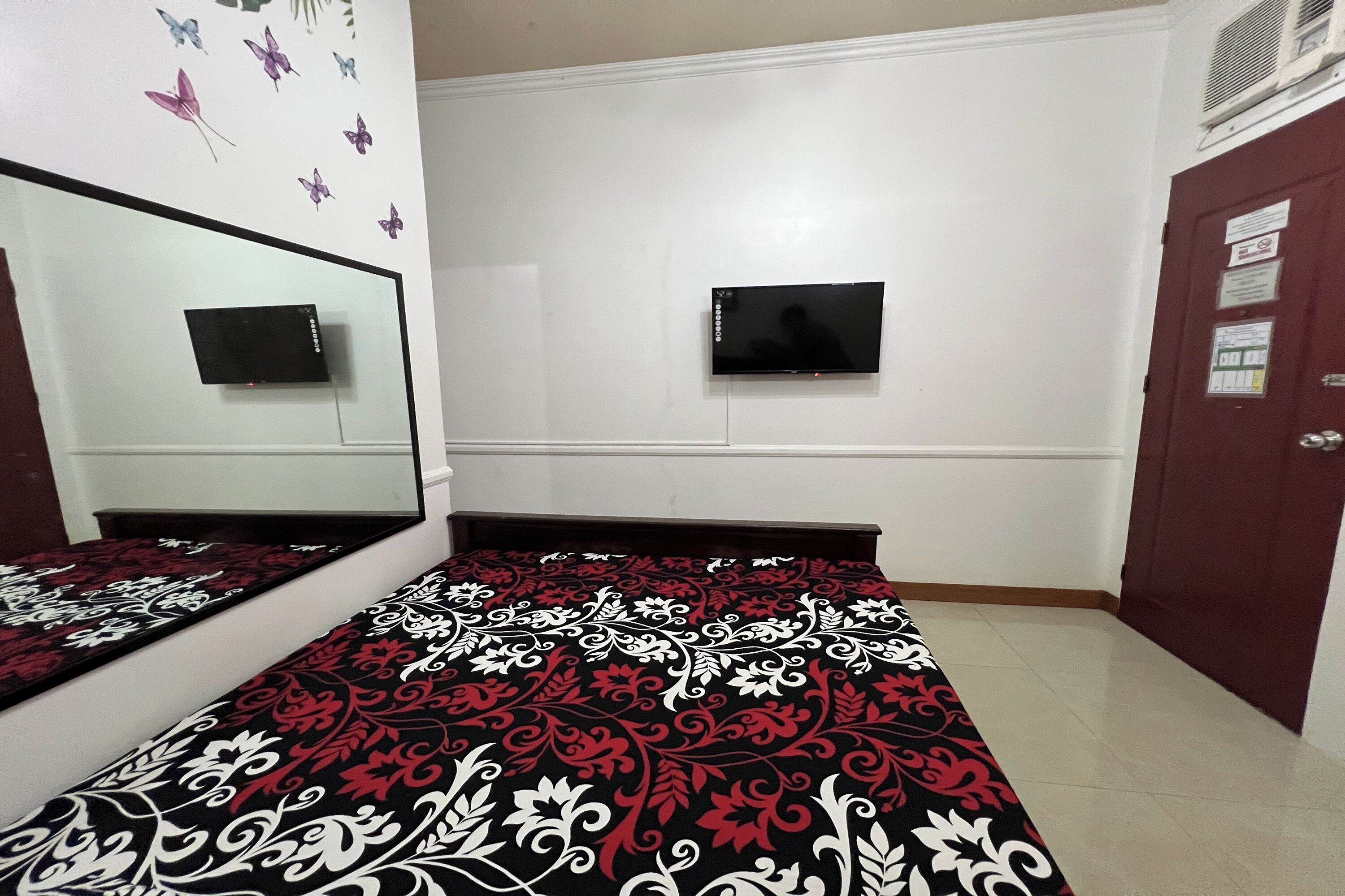 A bedroom with a bed, a mirror, a TV, and a door.
