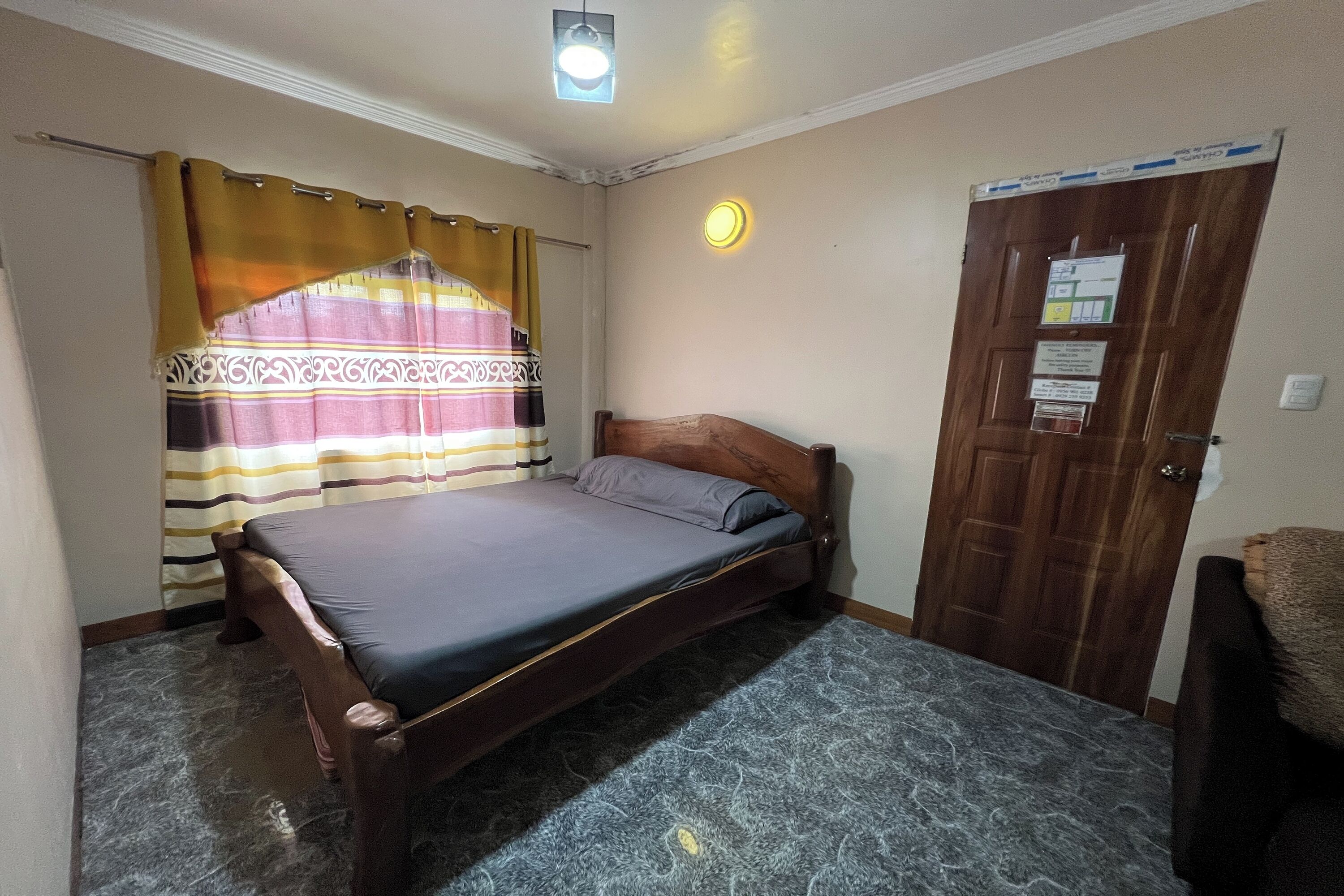 Un dormitorio con cama, cortinas, una puerta de madera y una lámpara.