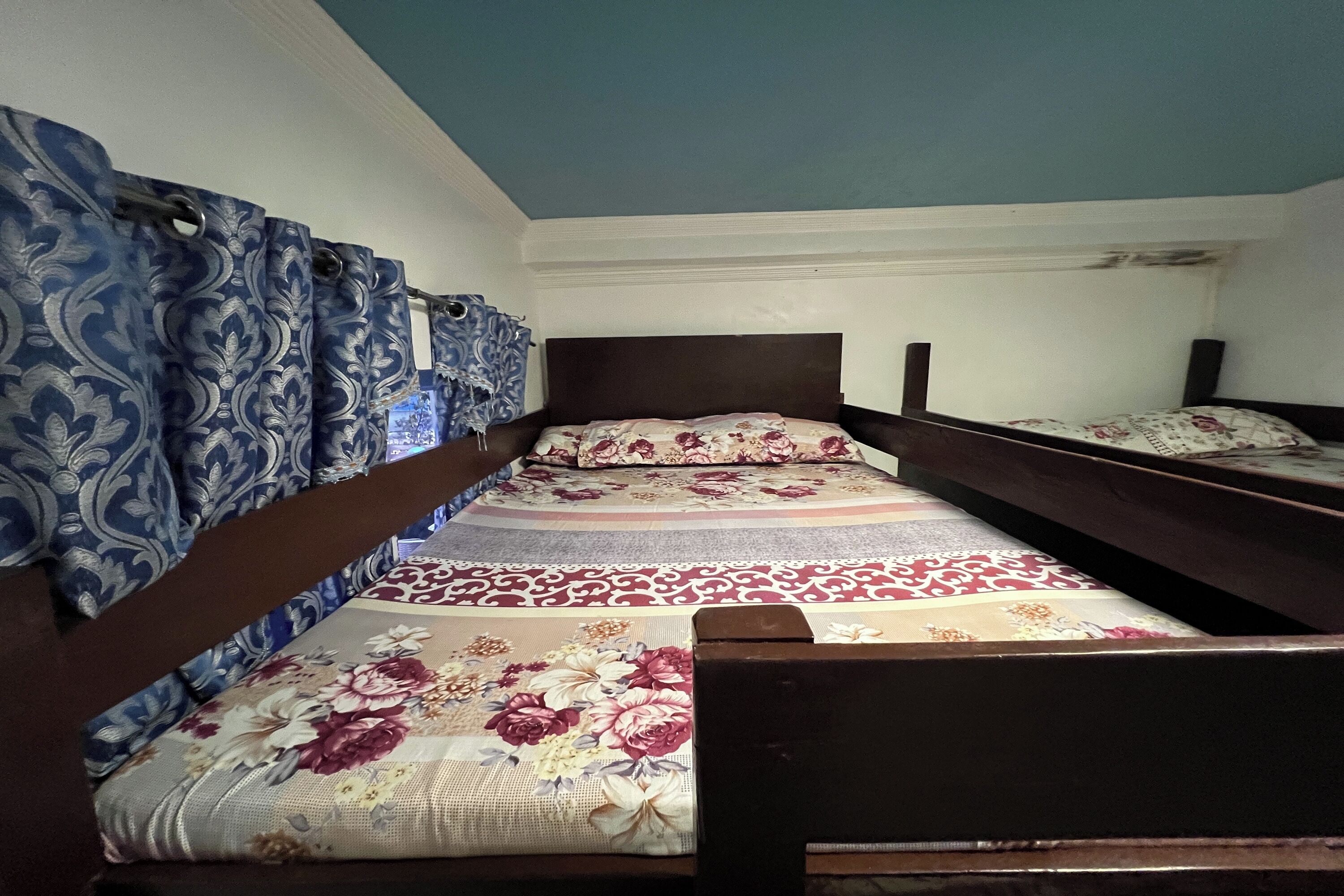 Een kamer met stapelbedden, bloemenbedrukking en blauwe gordijnen.