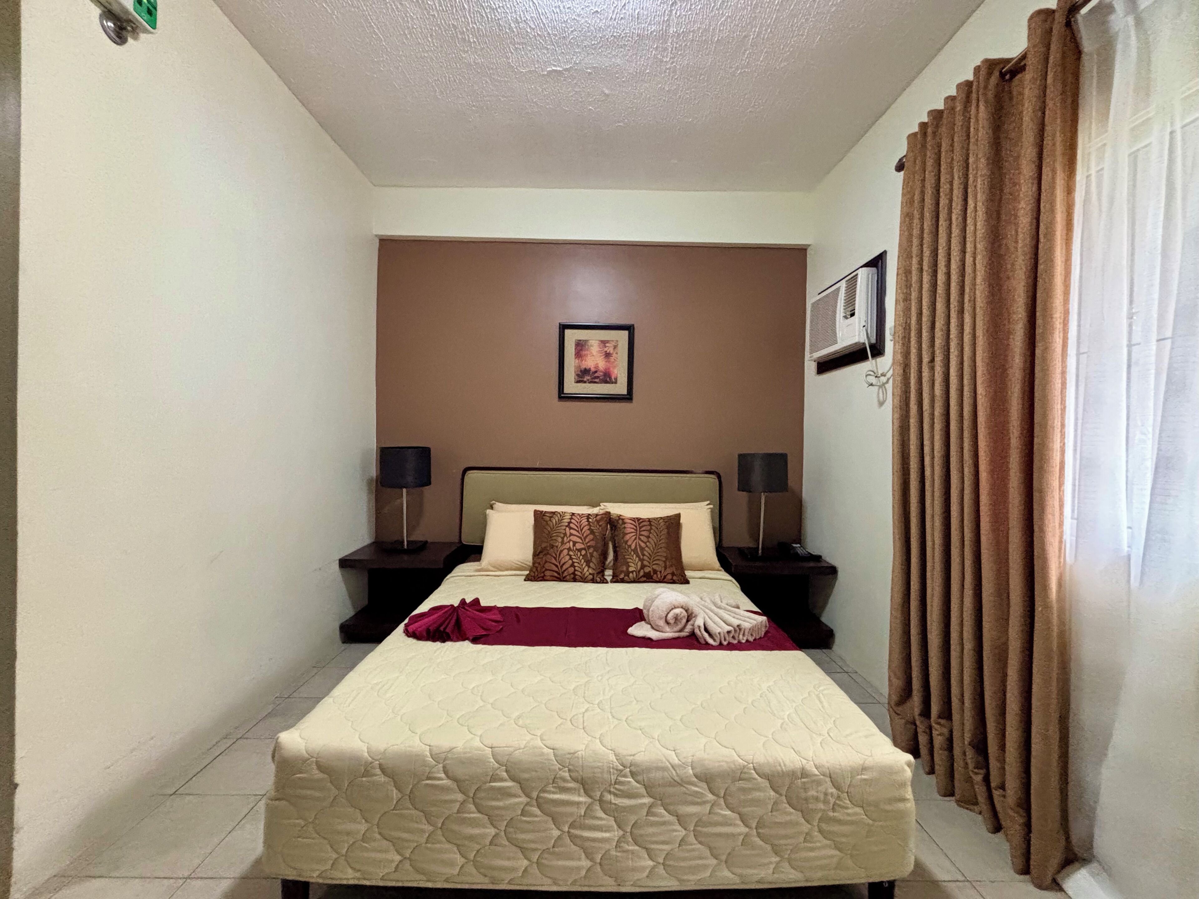 Habitación de hotel ordenada con cama, dos mesitas de noche, aire acondicionado de pared y cortina.