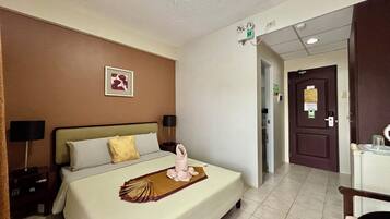 Habitación de hotel con una cama bien hecha, una lámpara de noche, un cuadro en la pared y una puerta con un cartel.