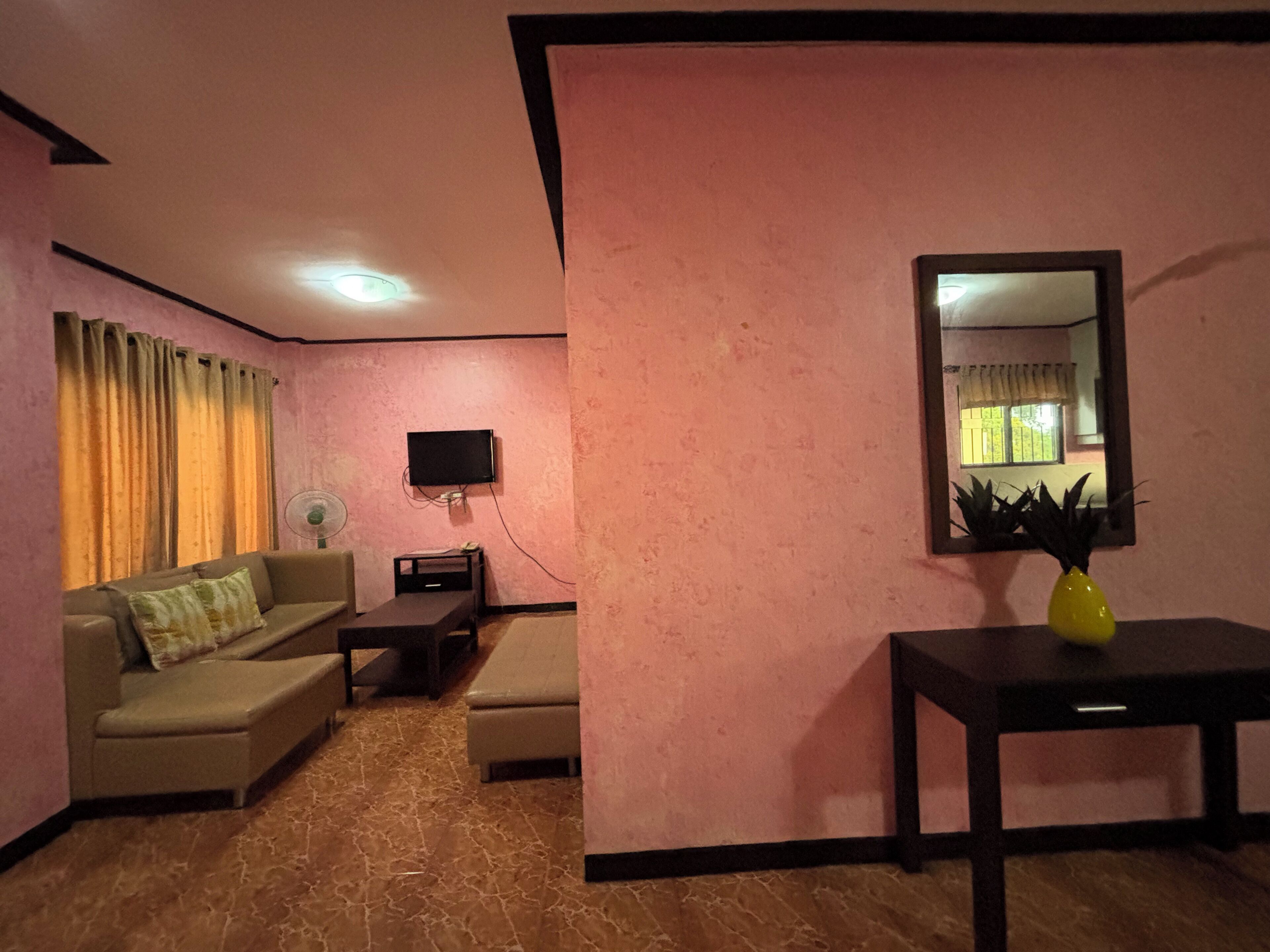 A living room with a sofa, a coffee table, a TV mounted on the wall, and a small table with a vase.