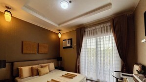 A hotel room with a large bed, a desk, and a window with curtains. - D' Leonor Inland Resort And Adventure Park (Davao)