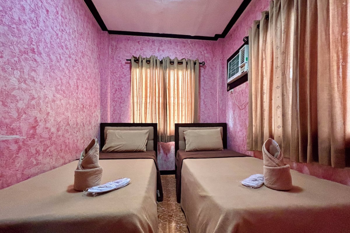 A room with two beds, pink walls, and a window with curtains.