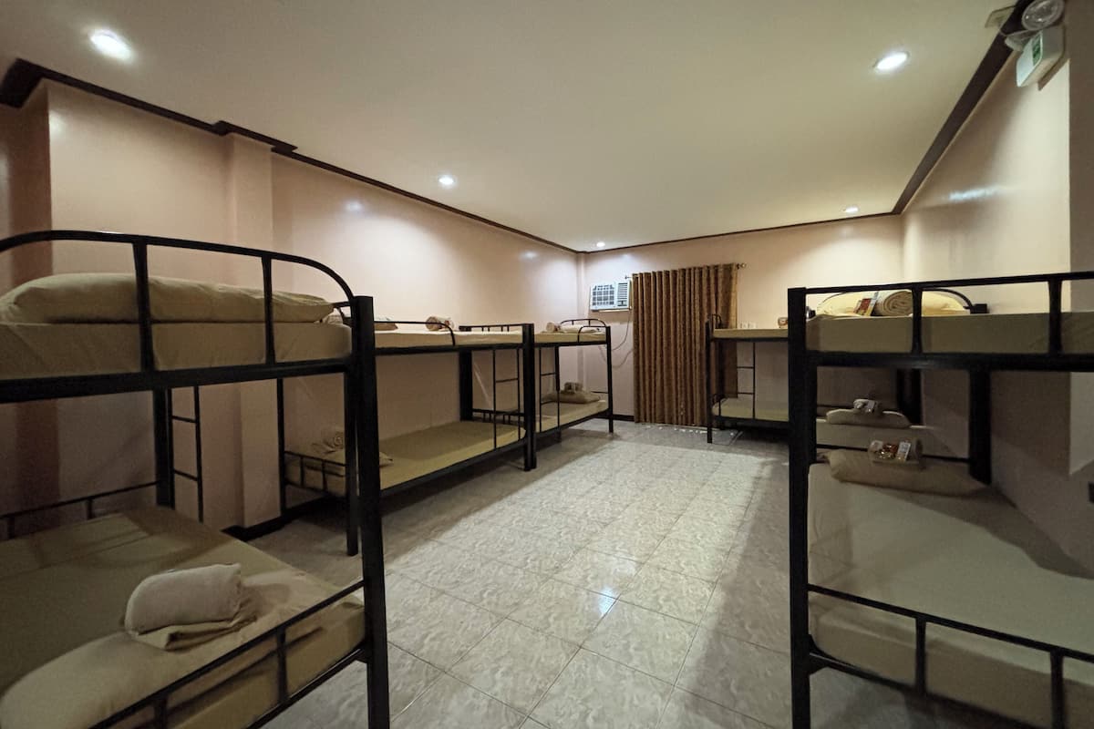 A dormitory room with bunk beds, a tiled floor, and a window with curtains.