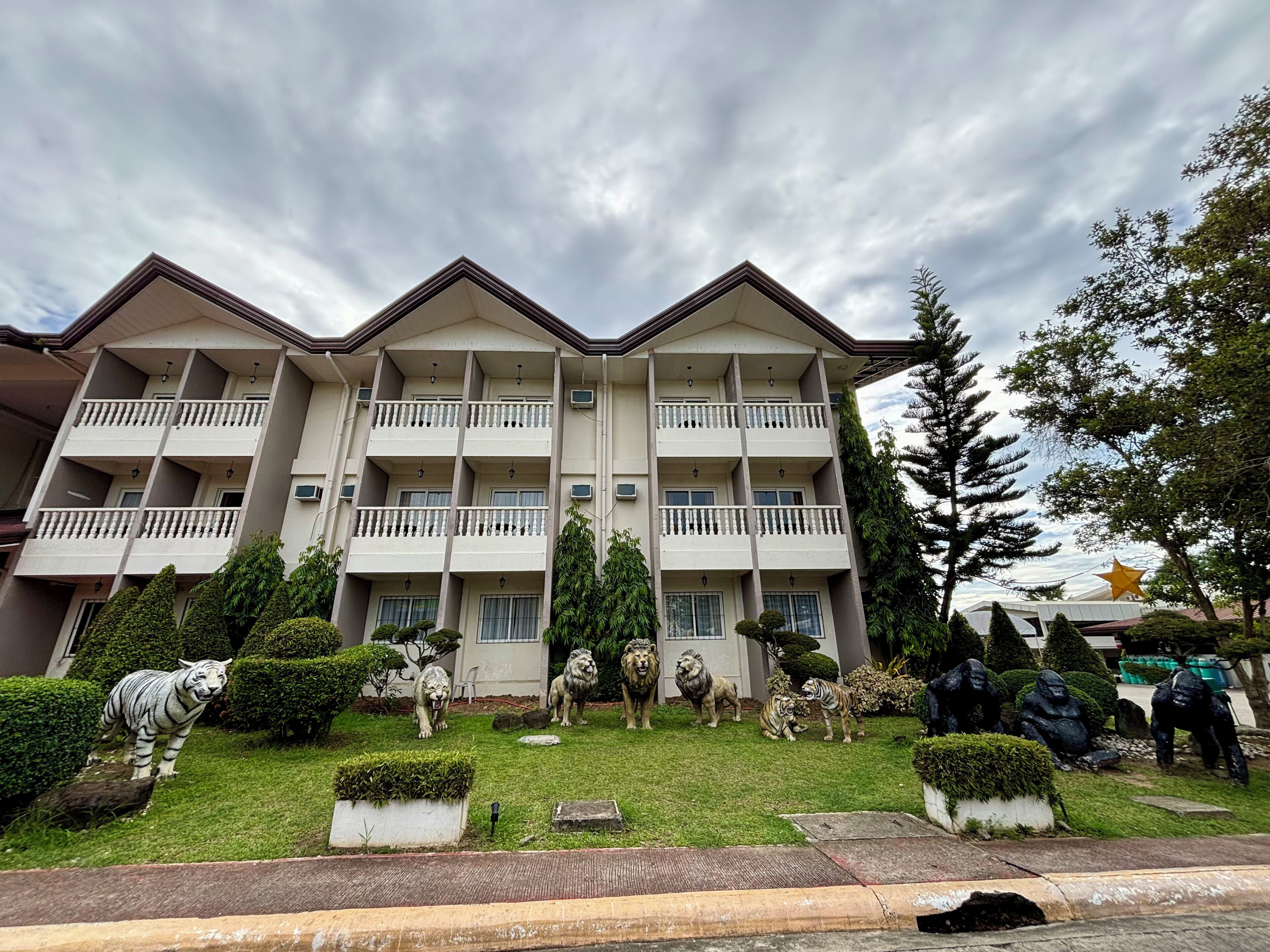 A multi-story hotel with balconies, a well-maintained lawn, and various statues.