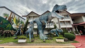 A large dinosaur statue in front of a hotel with multiple balconies and a garden. - D' Leonor Inland Resort And Adventure Park (Davao)