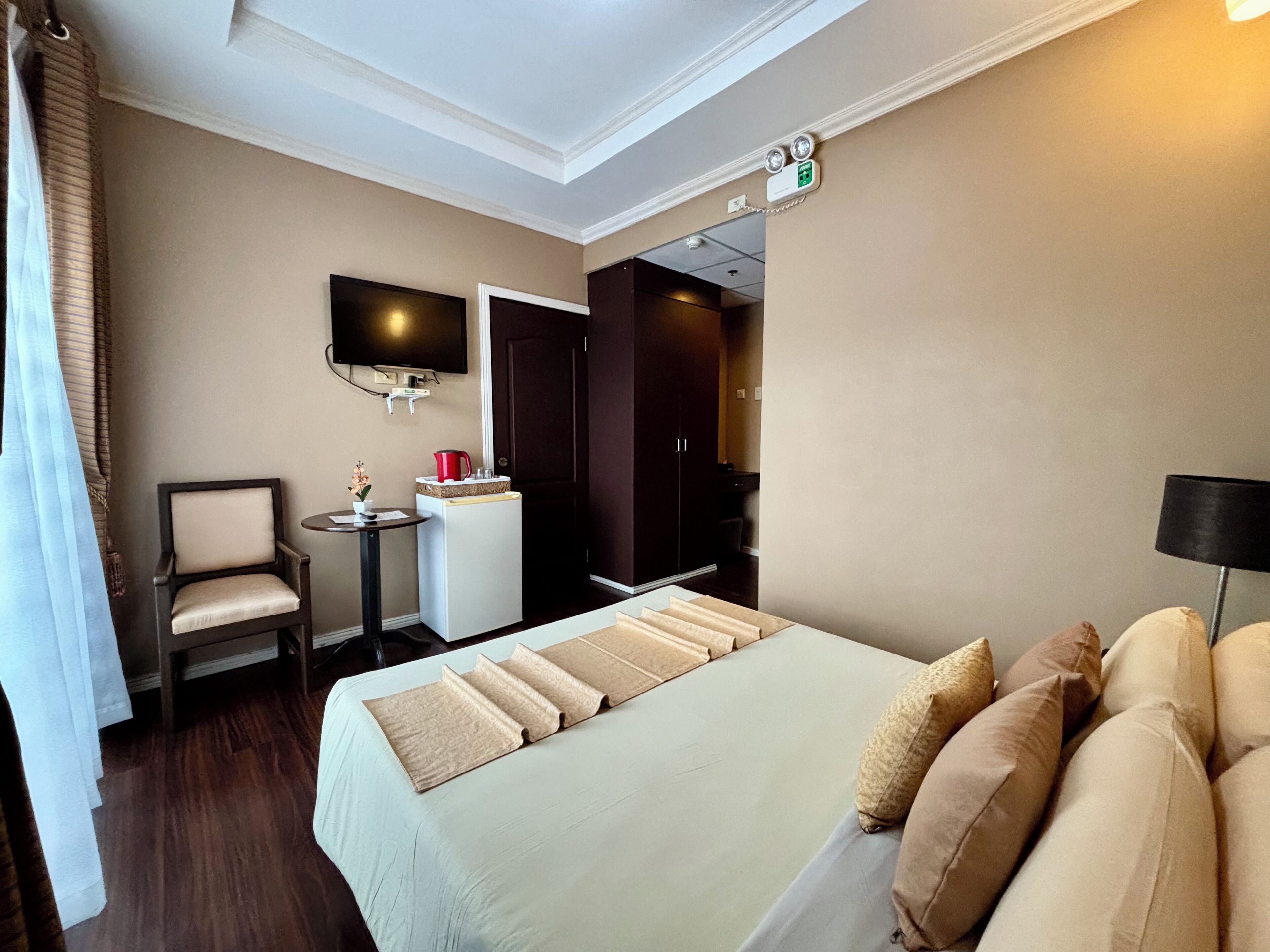 A hotel room with a bed, a chair, a small table, a TV, and a door leading to a bathroom.
