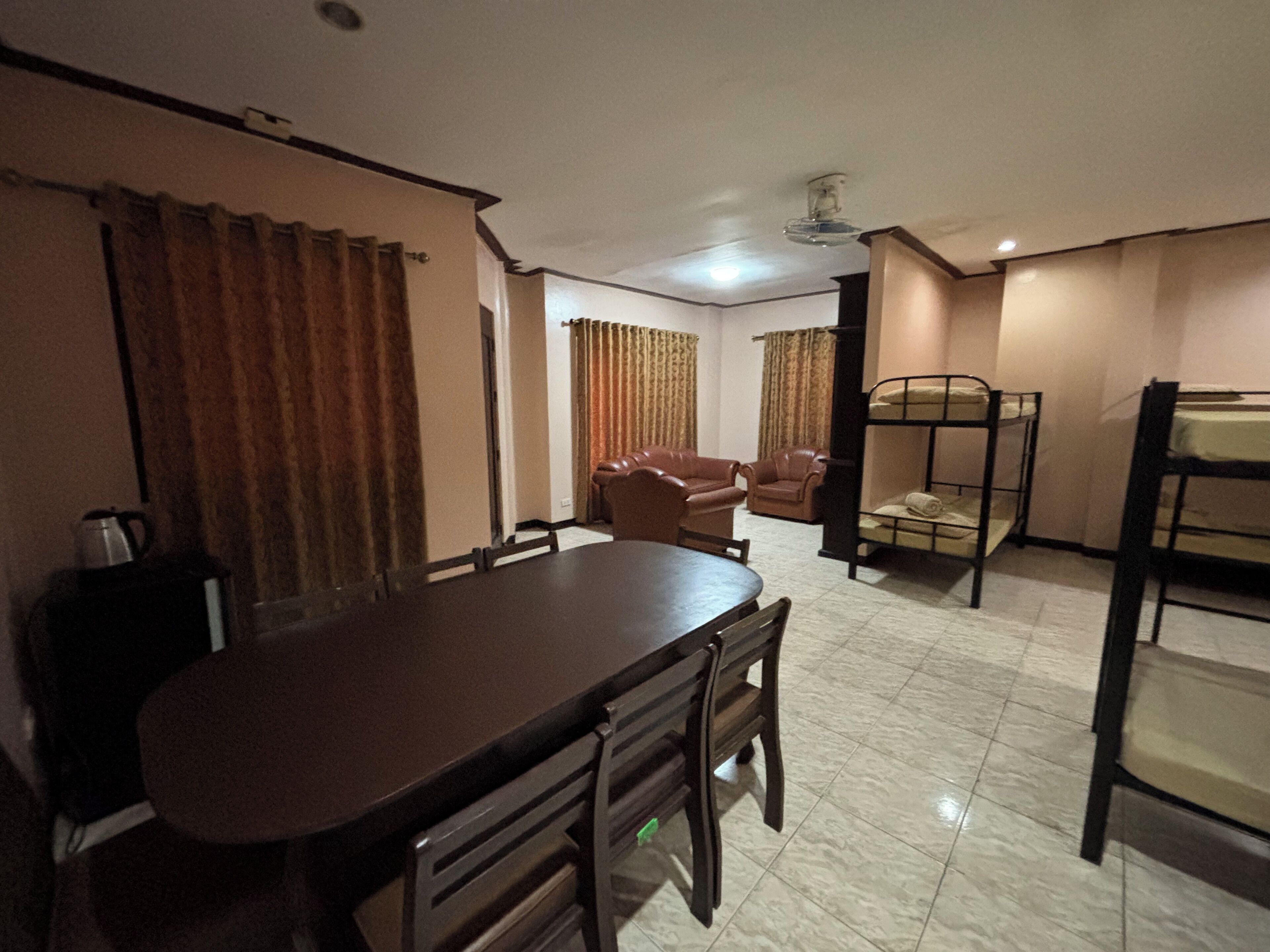 A room with a dining table, chairs, a bunk bed, and a sofa.