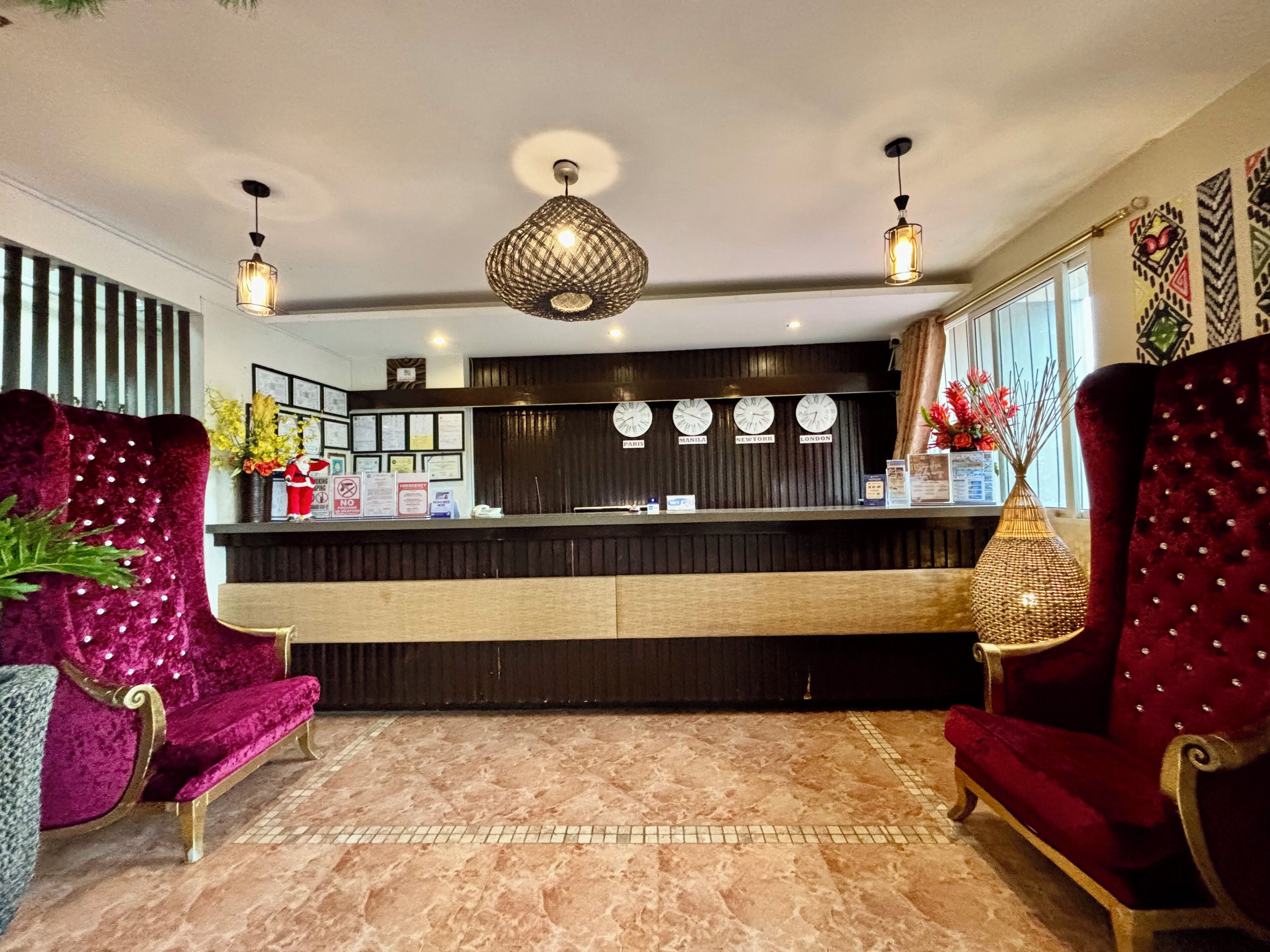A reception area with a marble floor, two red velvet armchairs, a black reception desk, and a decorative hanging light fixture.