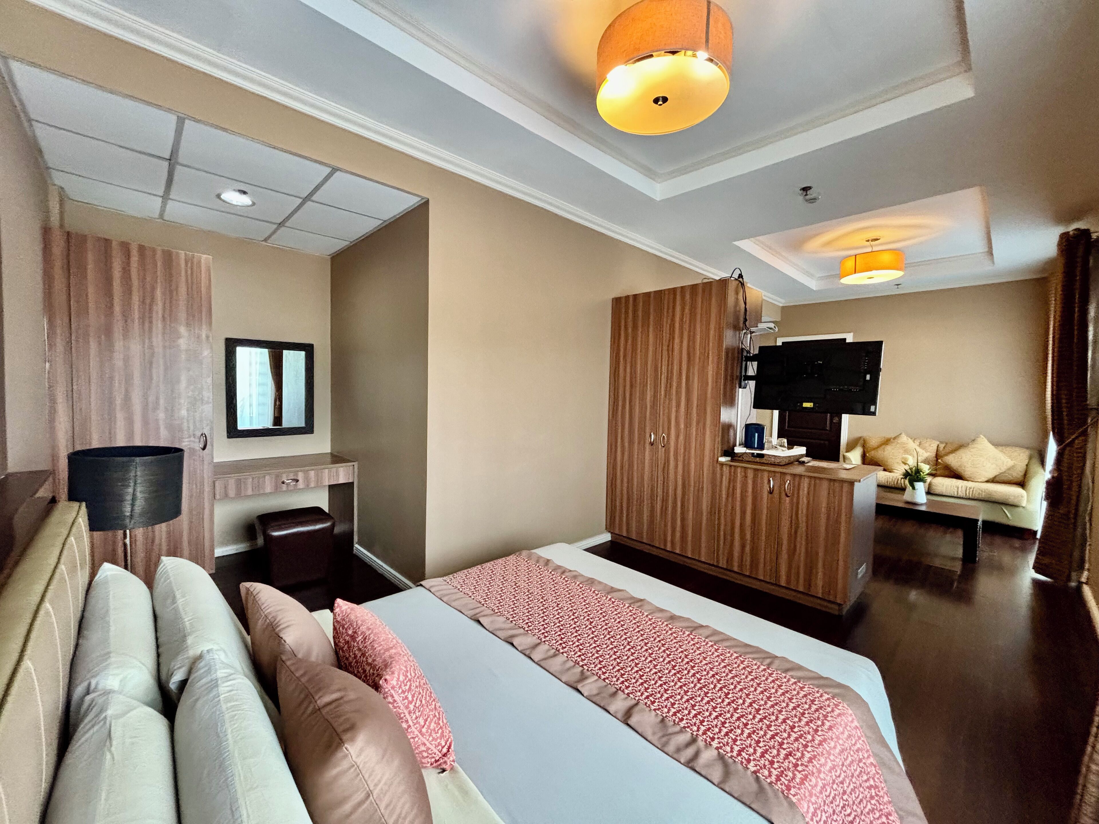 A hotel room with a large bed, a wooden wardrobe, a television, and a sofa.