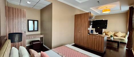 A hotel room with a large bed, a wooden wardrobe, a television, and a sofa.