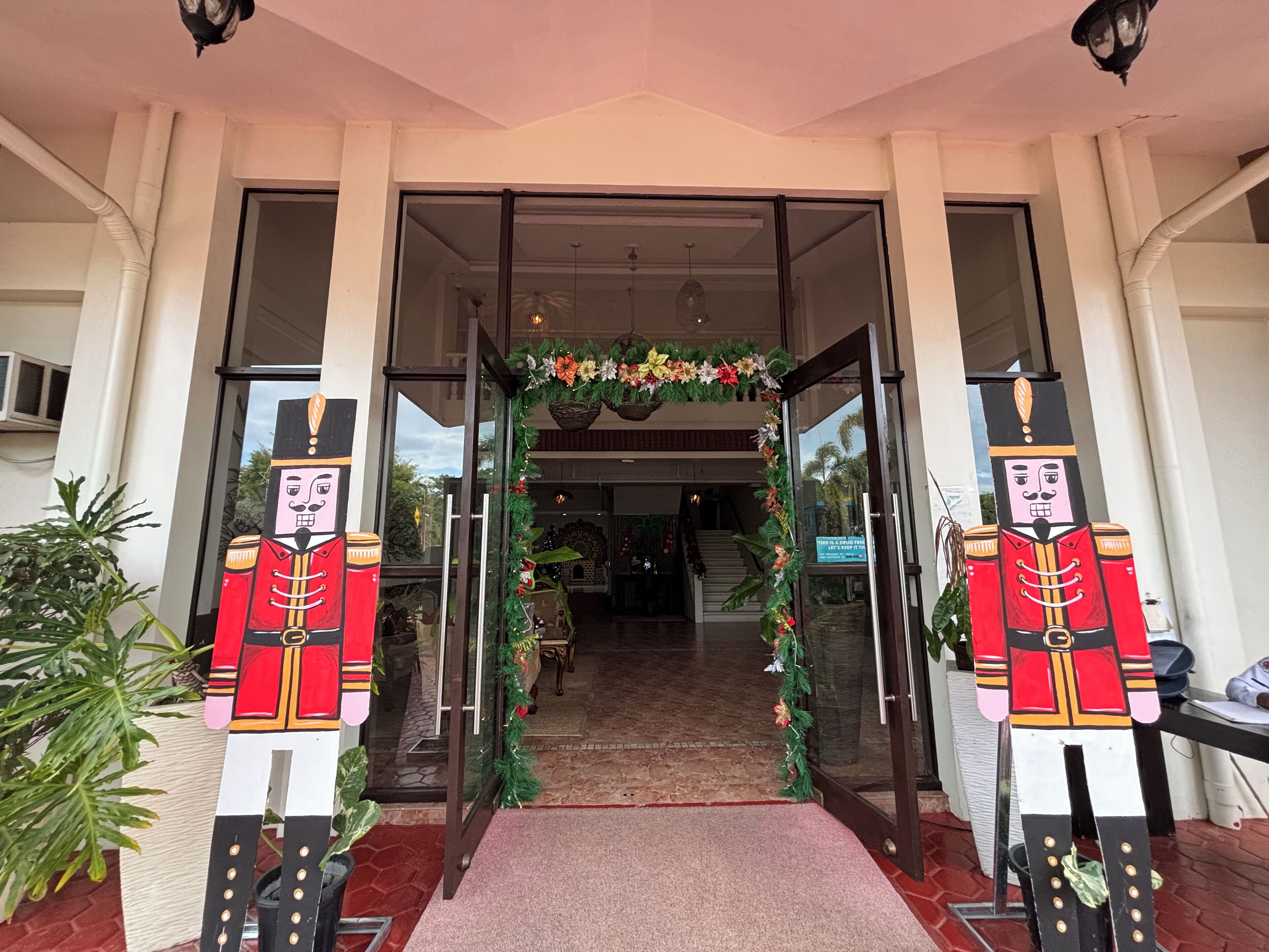 A hotel entrance with a glass door, a red carpet, and a festive wreath.