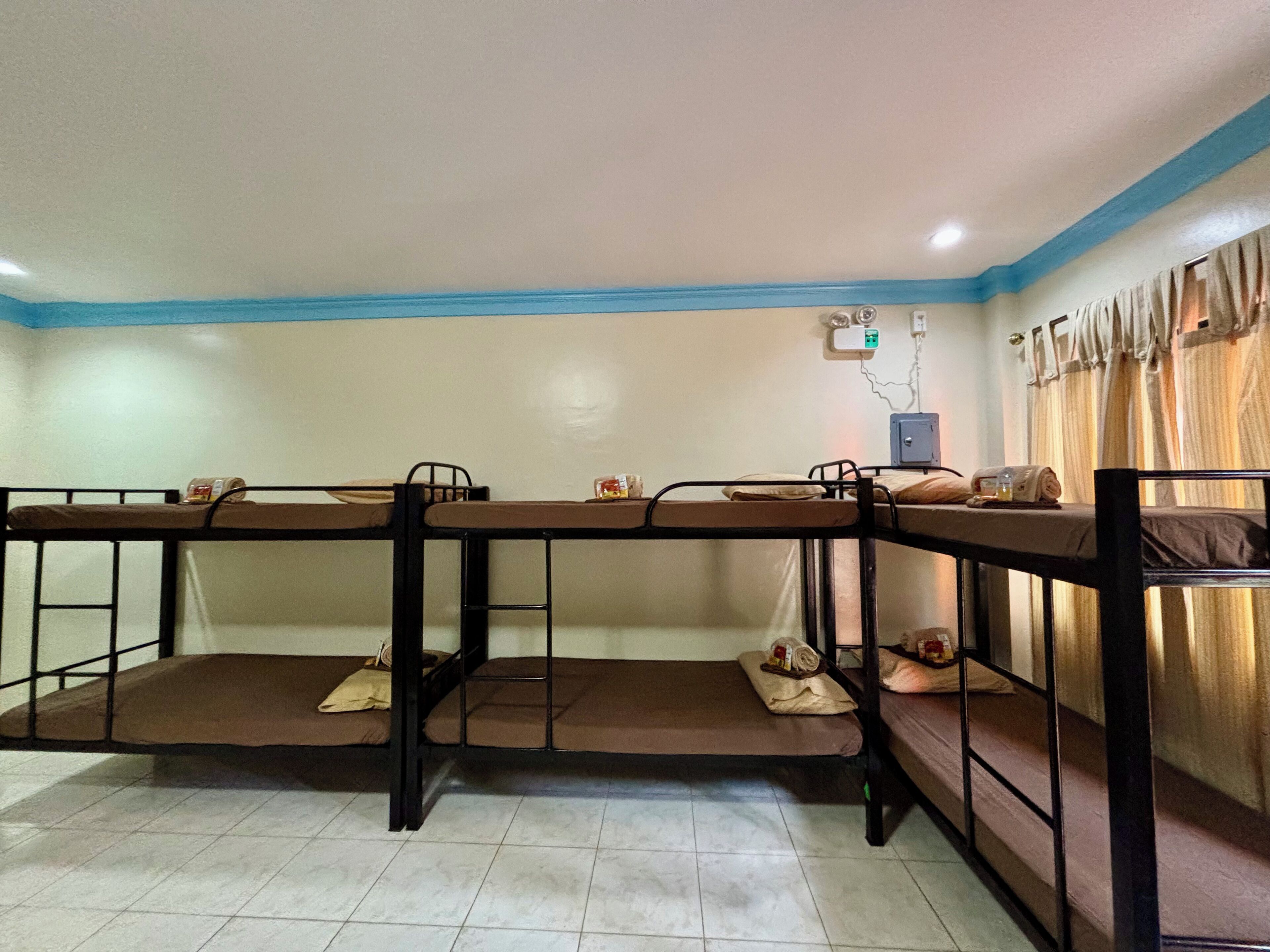 A dormitory room with bunk beds, a small table, and a power outlet on the wall.
