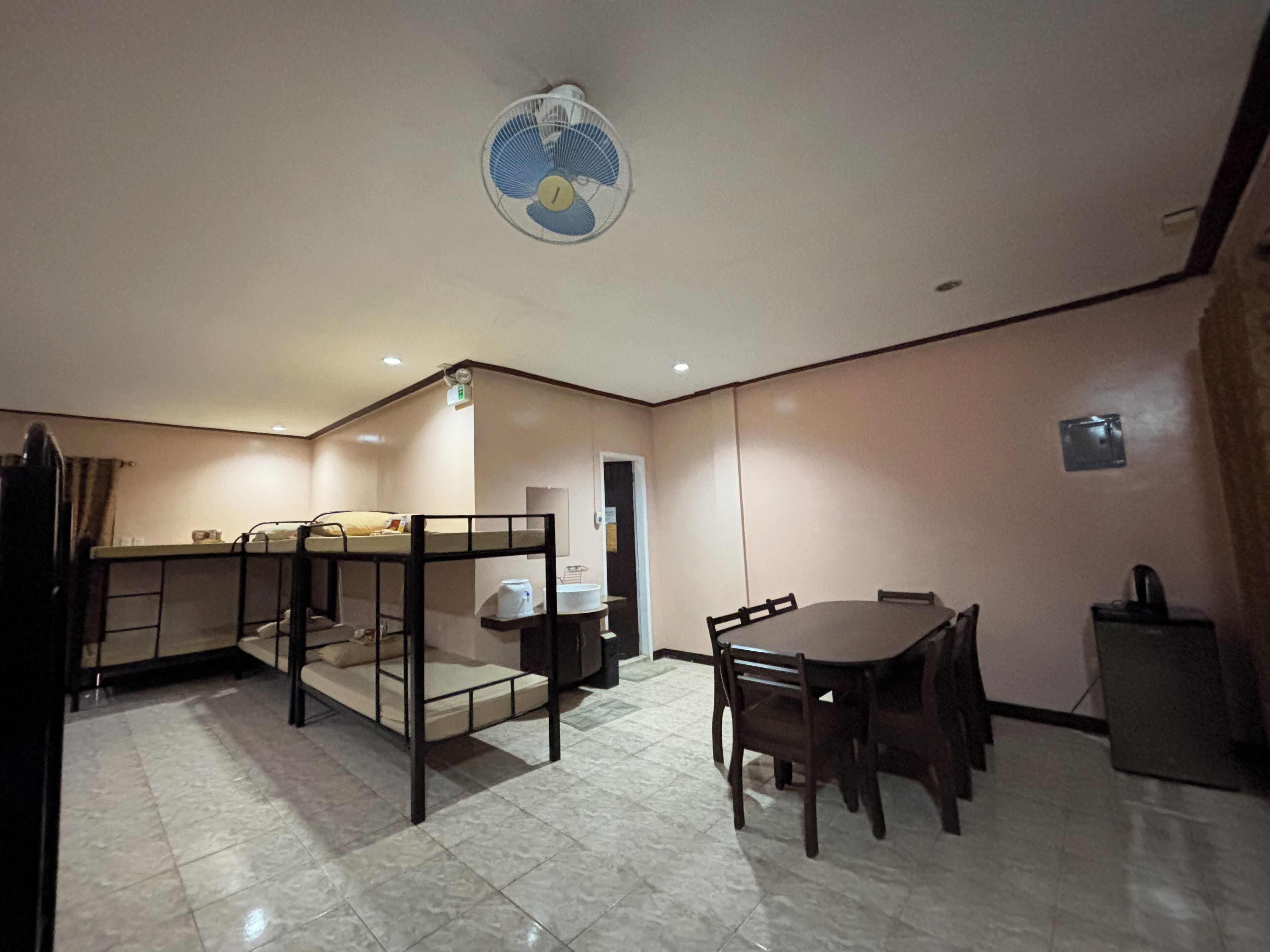A compact room with bunk beds, a dining table, and a ceiling fan.